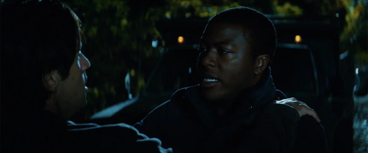 Red Dawn (2012) movie still: medium — A dark outdoor setting at night with a large vehicle partially visible behind men. One man stands facing…