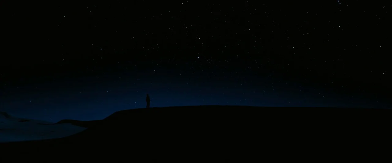 John Wick: Chapter 3 – Parabellum (2019) movie still: wide — A vast expanse of sand dunes sits under a clear night sky. A lone figure stands on the…