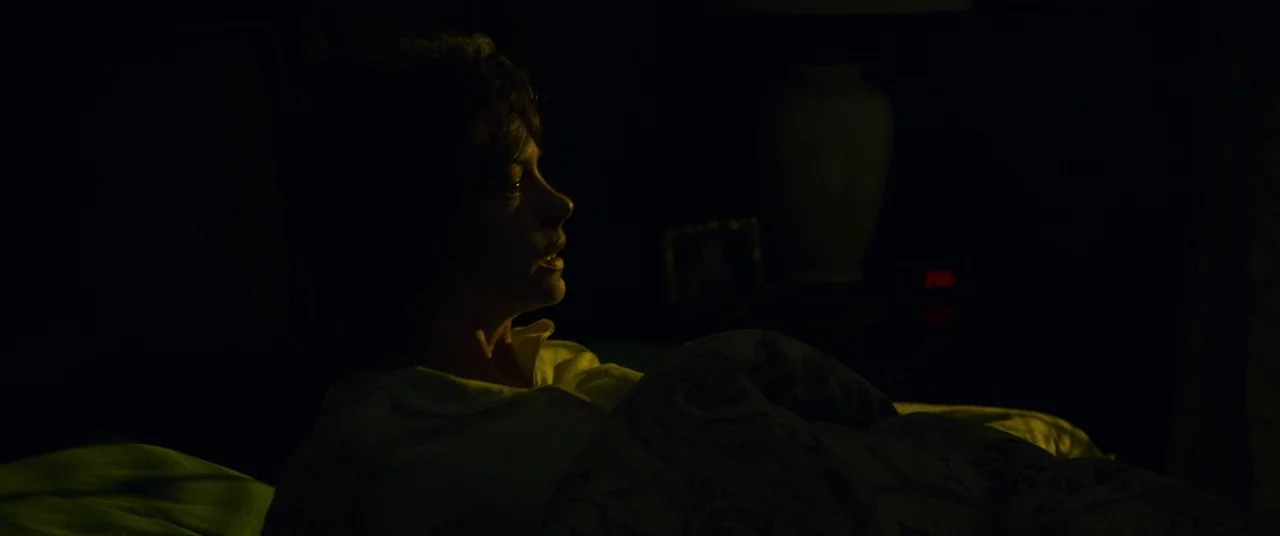Dark Waters (2019) movie still: medium — A dark, dimly lit bedroom at night with a table lamp in the background. A woman in a white collared shirt…