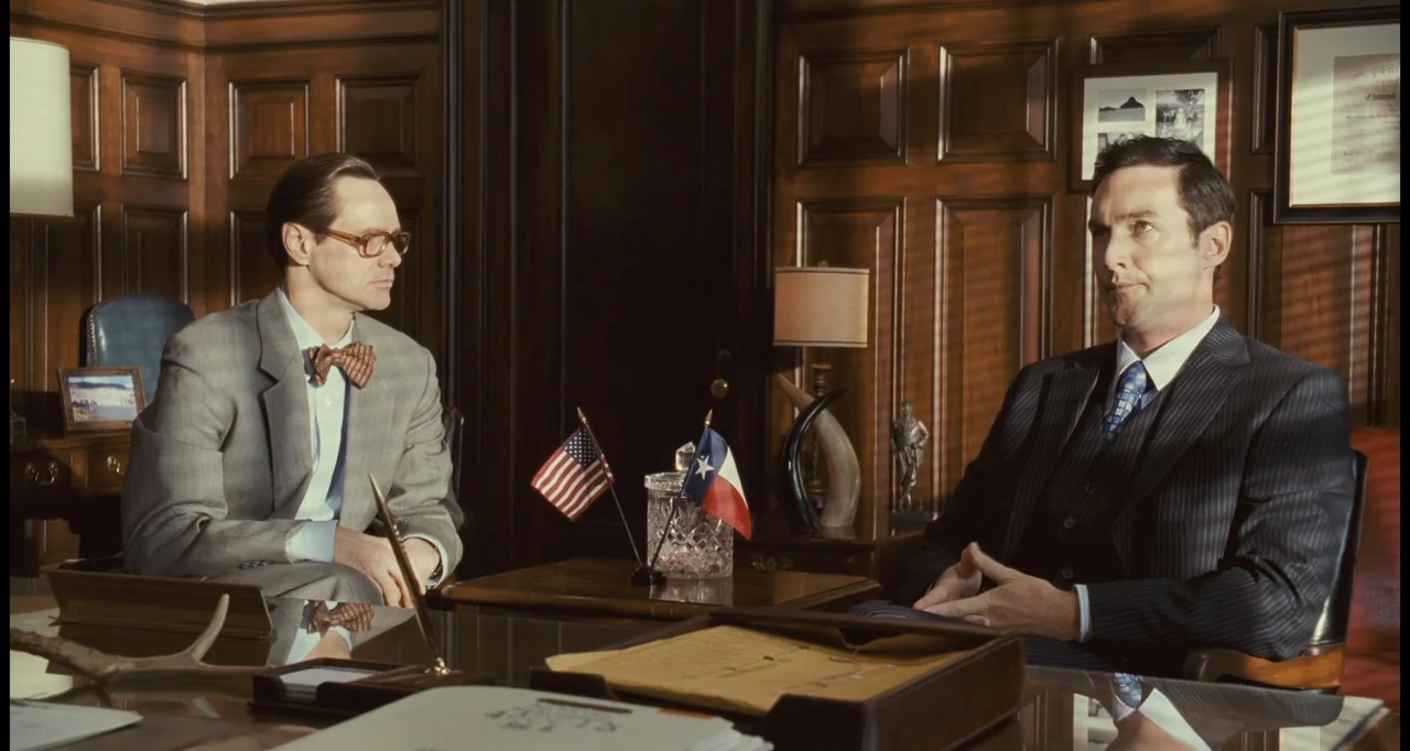 I Love You Phillip Morris (2010) movie still: medium — A wood-paneled executive office with flags and desk accessories sits in warm light. Two men…