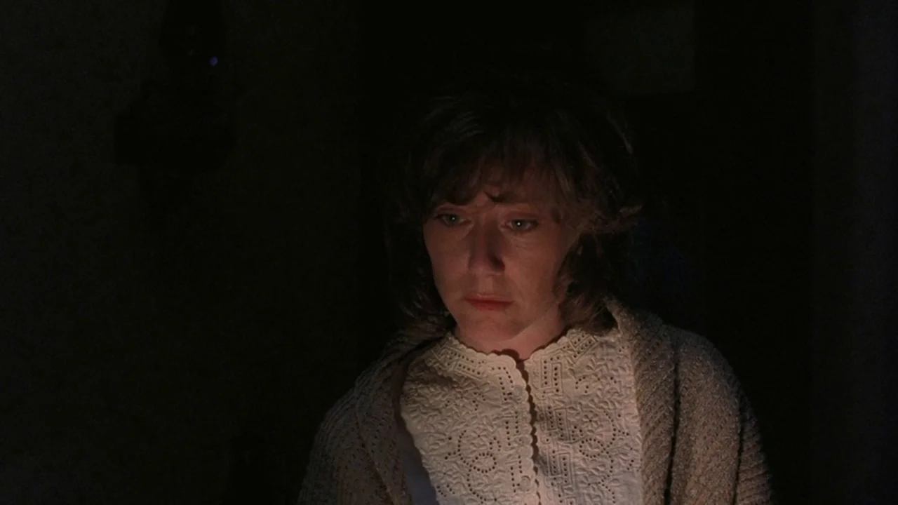 Matewan (1987) movie still: closeup — A woman stands in a dark room with minimal background detail visible. The subject stares downward with a…