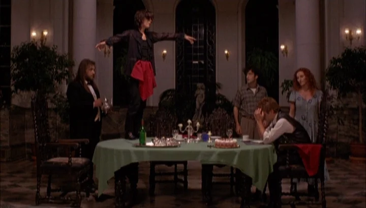 Highway 61 (1991) movie still: wide — A spacious formal hall features a round table draped with a green tablecloth. Five individuals stand or sit…
