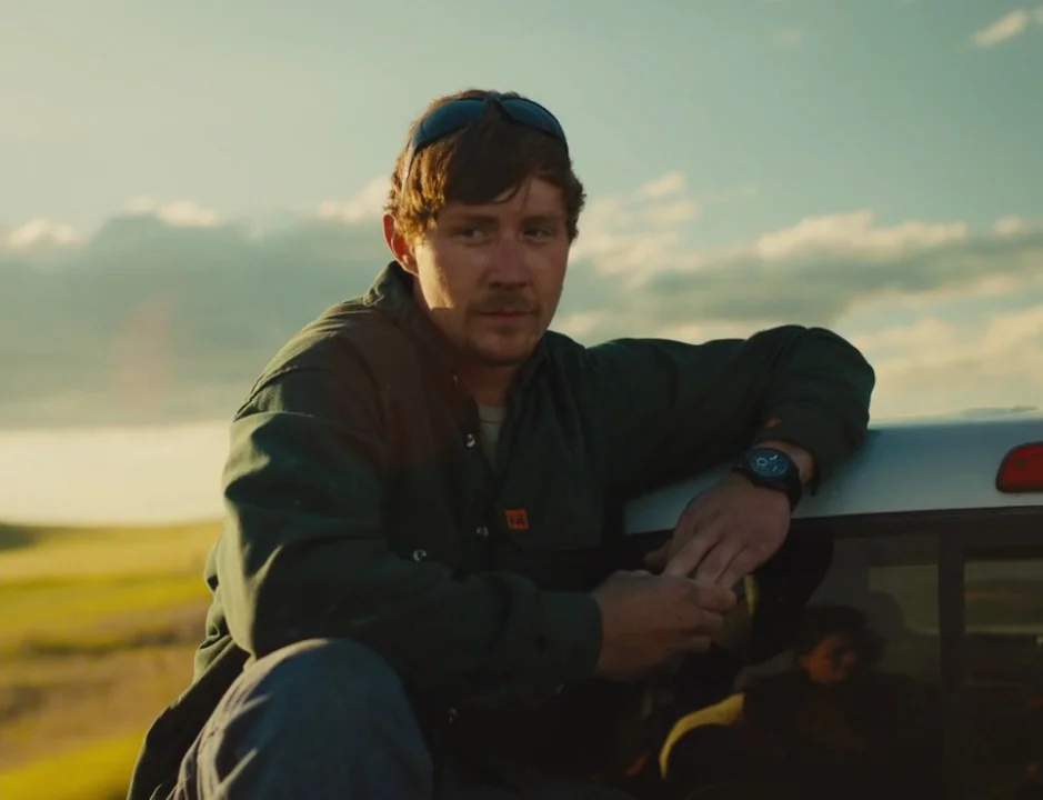American Honey (2016) movie still: medium — A man stands in an open rural field with golden sunlight behind him. He leans his left arm against the…