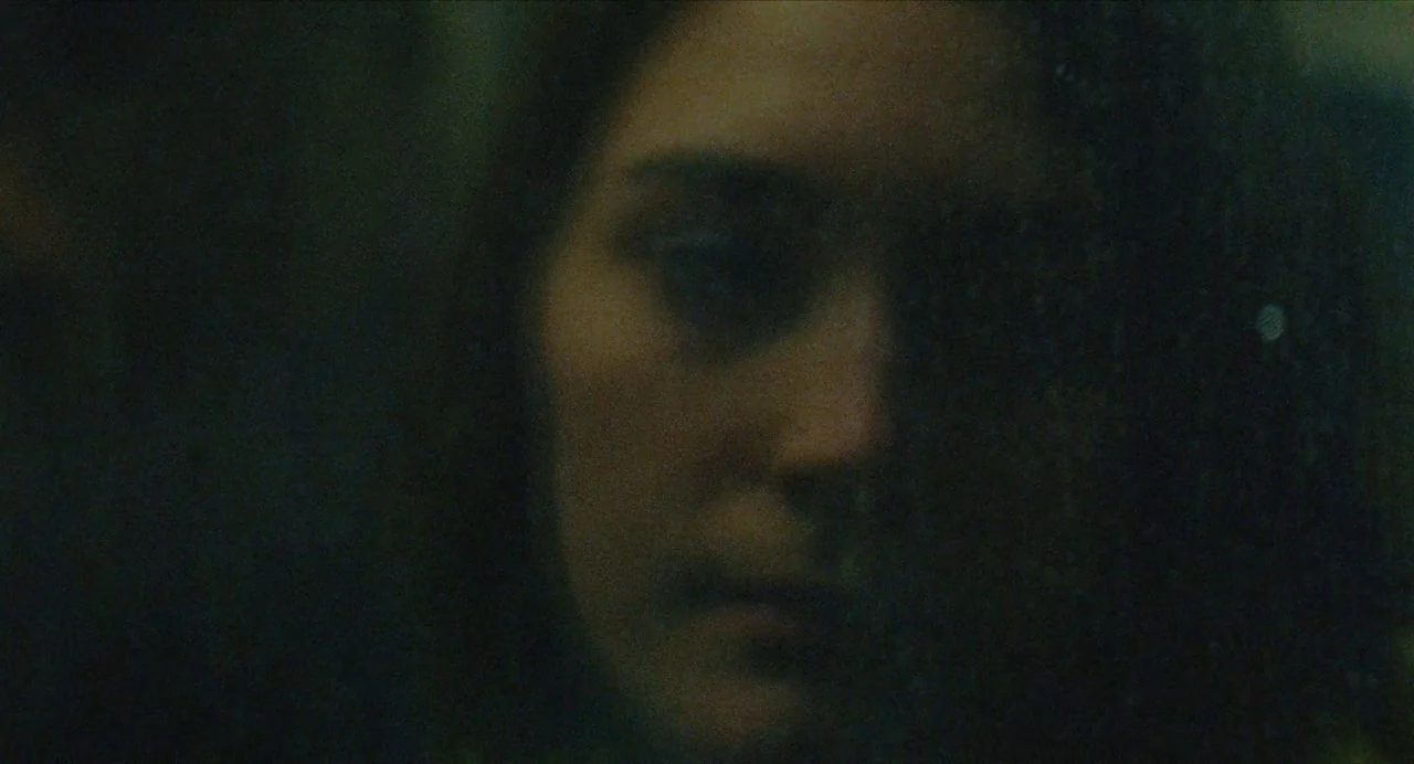Never Rarely Sometimes Always (2020) movie still: closeup — A close-up view through a dark, wet pane of glass. A woman looks through the window at…