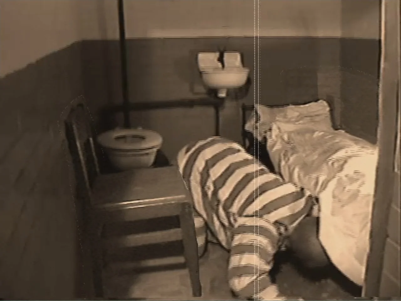 Dracula, Prisoner of Frankenstein (1972) movie still: medium — A cramped and sparse room with a metal frame bed and toilet fixture. A person in…