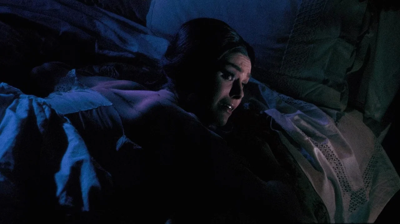 The Whip and The Body (1963) movie still: closeup — A woman lies on a bed under dark sheets with lace-trimmed linens. She looks toward the side of…