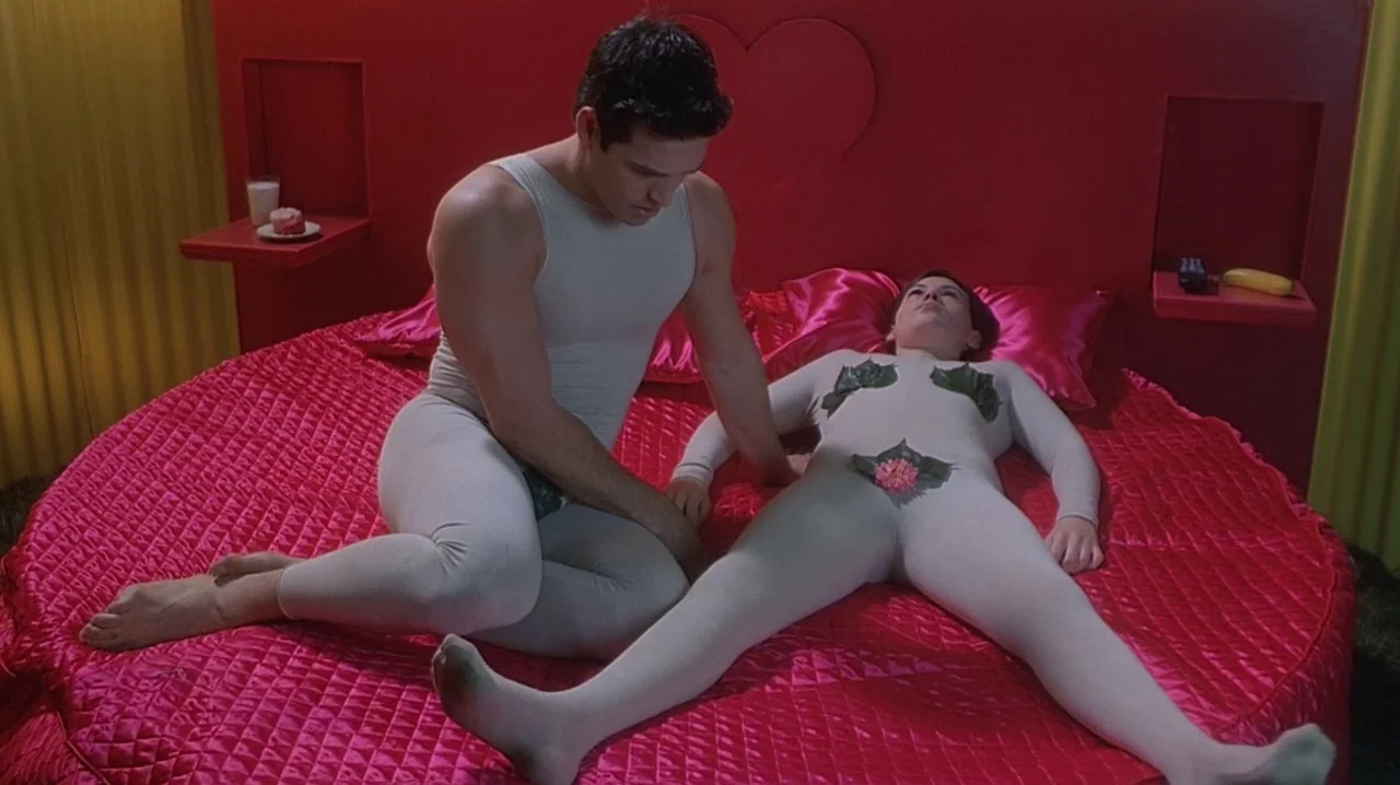 But I’m A Cheerleader (1999) movie still: medium — A circular red bed sits against a matching red wall with a heart cutout. Two individuals in white…