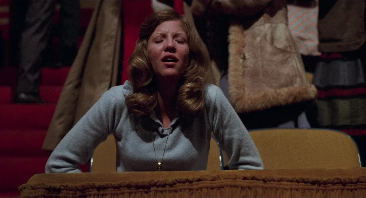 I Wanna Hold Your Hand (1978) movie still: medium — A dark indoor setting features rows of seating with a woman positioned in foreground. The woman…