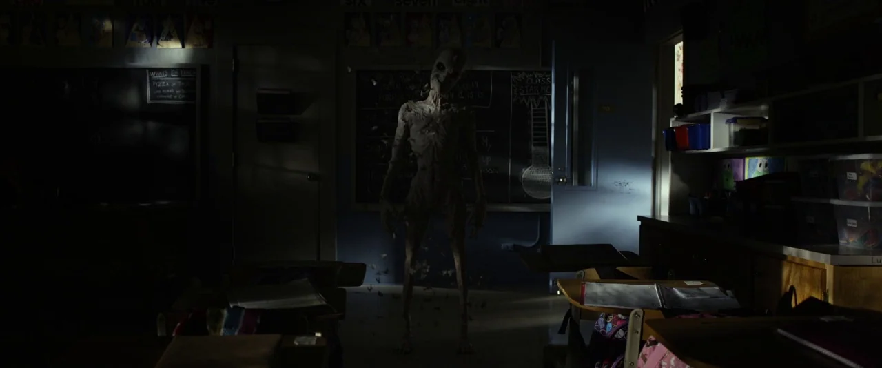 Before I Wake (2016) movie still: fullbody — An elementary school classroom is dimly lit, with desks scattered and charts on walls. A pale emaciated…
