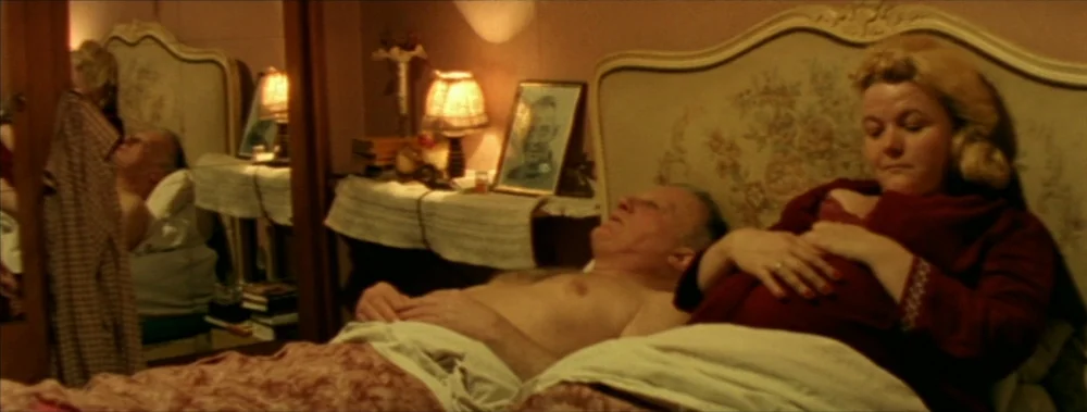 I Stand Alone (Seul Contre Tous) (1998) movie still: medium — A dimly lit room features a bed with an ornate wooden headboard. An elderly man and a…