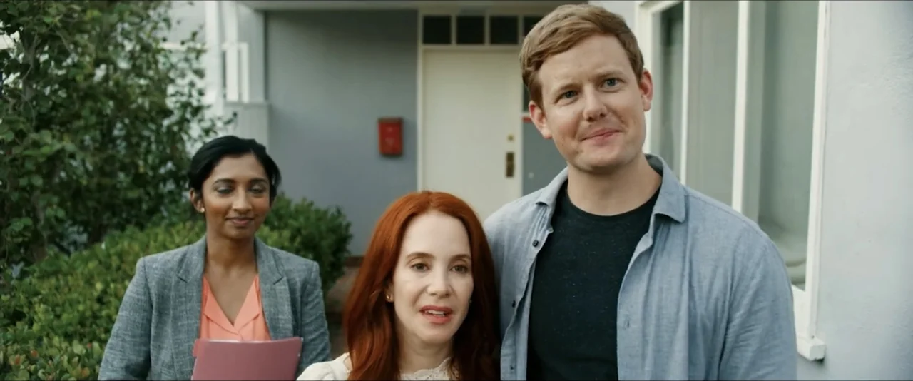 Gatlopp: Hell of a Game (2022) movie still: medium — The exterior of a house entrance with grey walls and a white door. Three adults stand together…