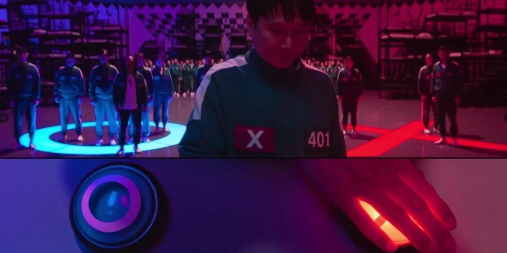 Squid Game (2024) movie still: medium — A dark dormitory space contains tiered bunk beds and illuminated colored floor markings. A man stands in the…