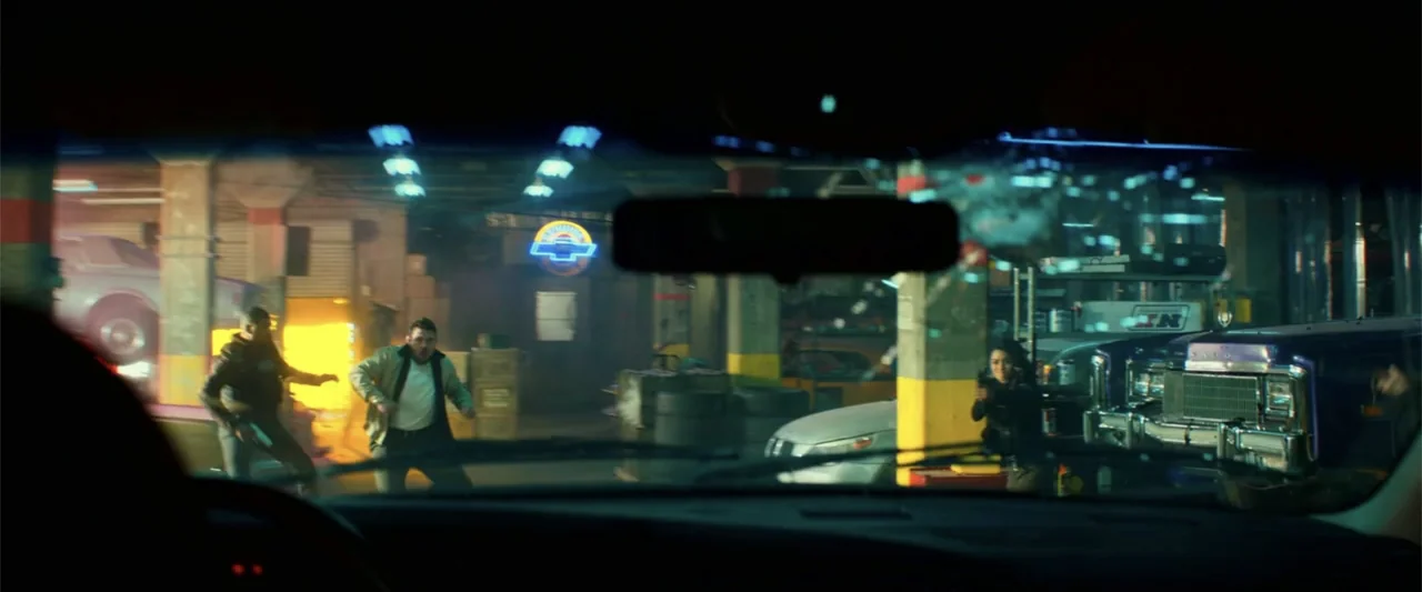 Bad Boys for Life (2020) movie still: wide — A cluttered auto repair shop with vintage vehicles and industrial tools visible throughout. Two men and…