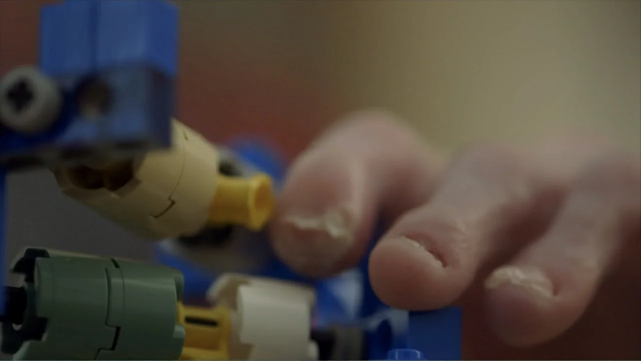 Life According to Sam (2013) movie still: closeup — A close view of human fingers interacting with colorful plastic construction toy pieces. The…