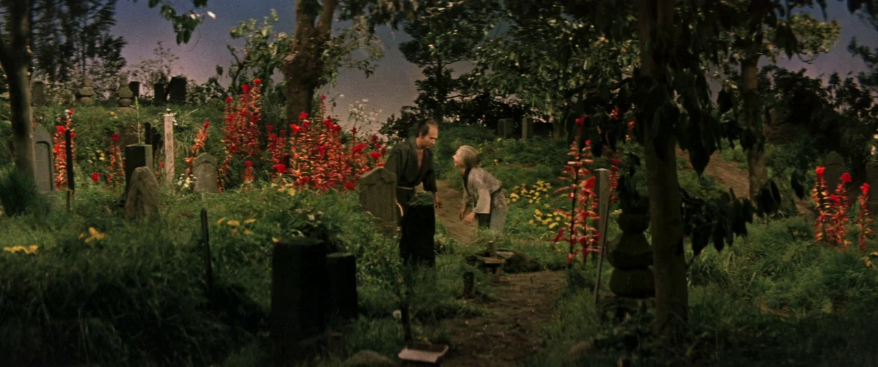 Ballad Of Narayama (1958) movie still: wide — An outdoor burial site features stone markers nestled among thick, vibrant green grass and flowers. A…