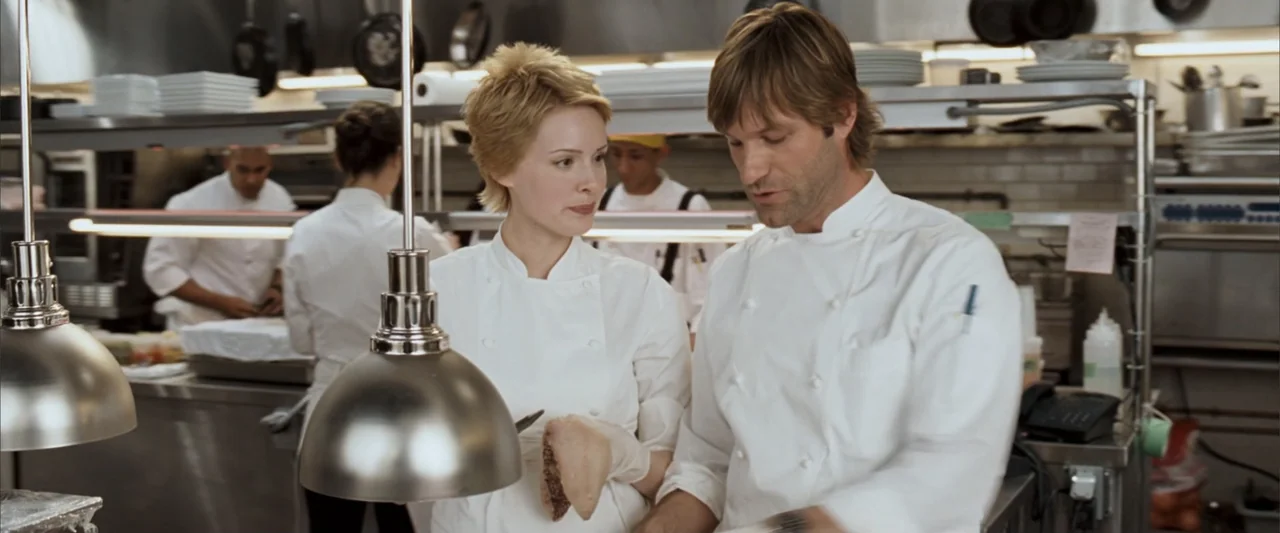 No Reservations (2007) movie still: medium — A commercial kitchen with stainless steel workstations and hanging heat lamps. Two chefs discuss…