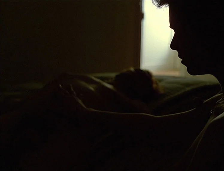 First Name: Carmen (1983) movie still: medium — A dark bedroom with a person in the foreground seen in profile silhouette. The subject reaches…