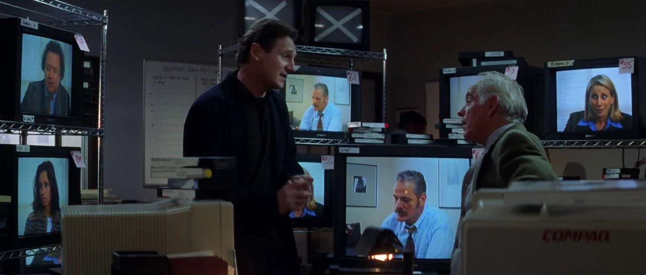 The Haunting (1999) movie still: medium — A dimly lit room is filled with shelves stacked high with multiple CRT monitors. Two men stand in the…