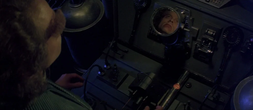 Dune (1984) movie still: medium — A dark, cramped control station features a complex mechanical console with various levers and buttons. A man…