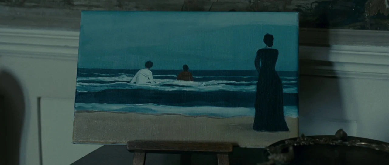 The Woman in Black (2012) movie still: closeup — A framed oil painting rests on a small wooden easel against a white wall. The artwork shows a woman…