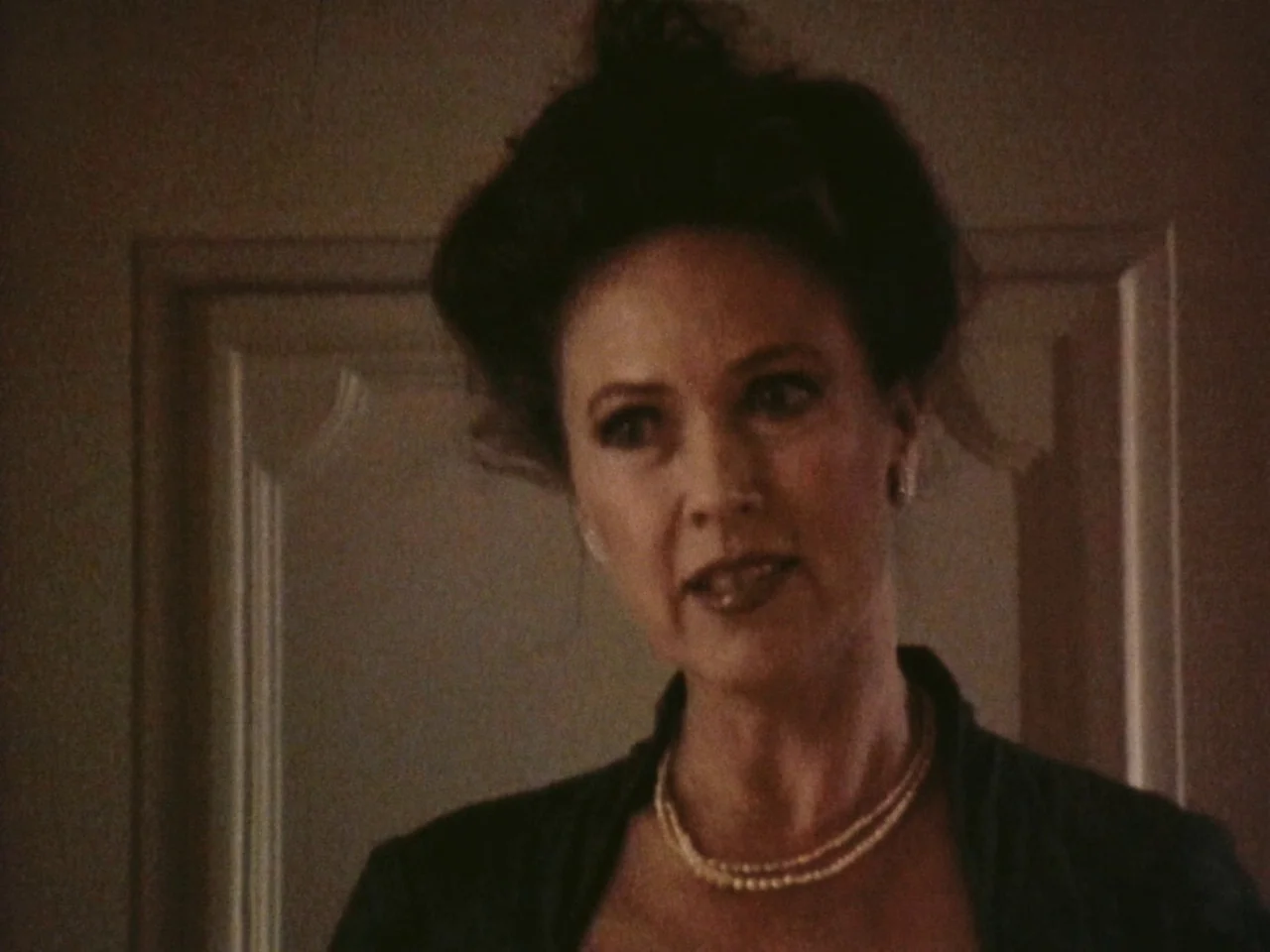 Festen (1998) movie still: closeup — A dimly lit interior space features a woman framed against a panelled wall. She speaks while looking toward the…