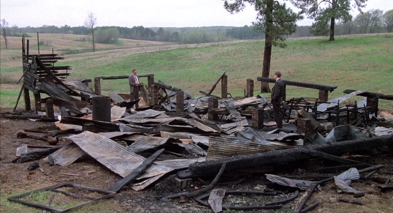 Mississippi Burning (1988) movie still: wide — A rural landscape features the smoldering, debris-filled remains of a demolished wooden building. Two…