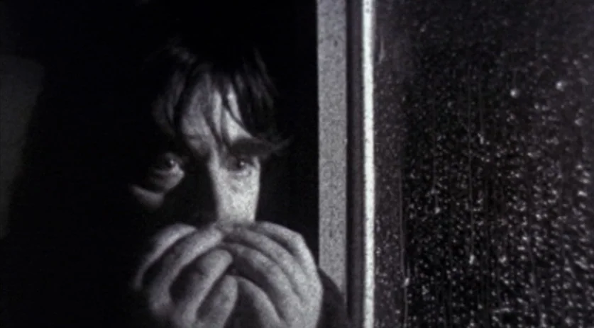 The Saddest Music in the World (2003) movie still: closeup — A dimly lit interior space with a windowpane covered in heavy rain droplets. A man sits…