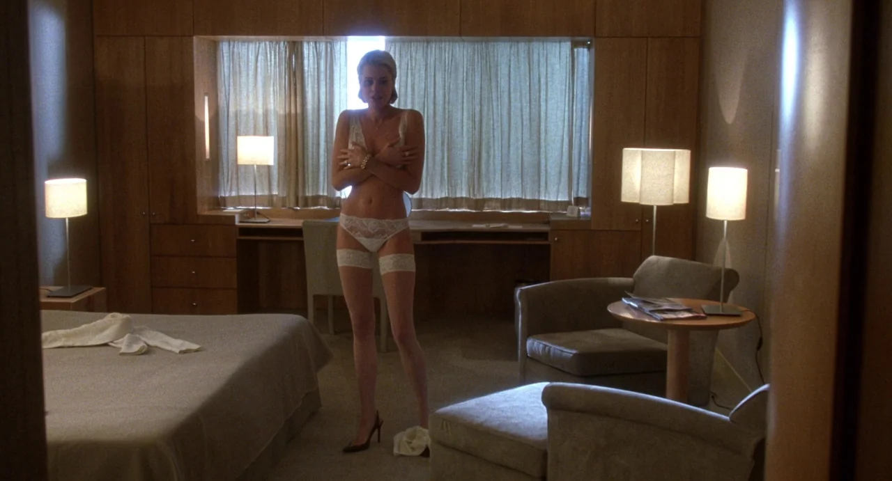 Femme Fatale (2002) movie still: fullbody — A modern hotel room features light wood paneling, floor-to-ceiling curtains, and matching beige…