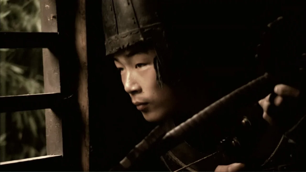 The First Emperor (2006) movie still: closeup — A dark, cramped wooden room with a window covered by horizontal slats. A young man wearing a helmet…