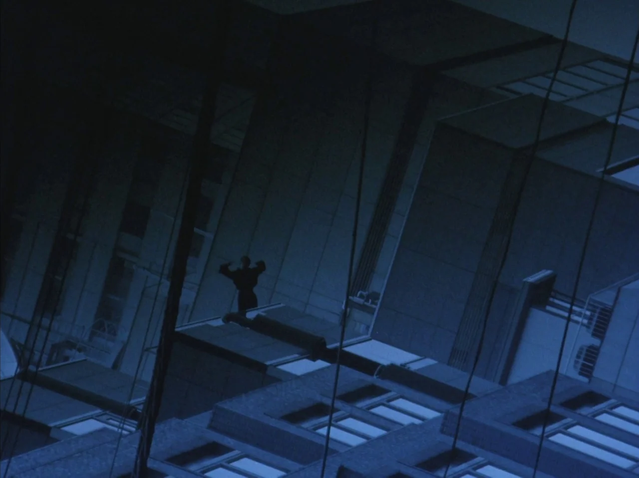 Tetsuo II: Body Hammer (1992) movie still: wide — A dark, angled reflection of a multi-story building occupies most of the frame. A lone figure…
