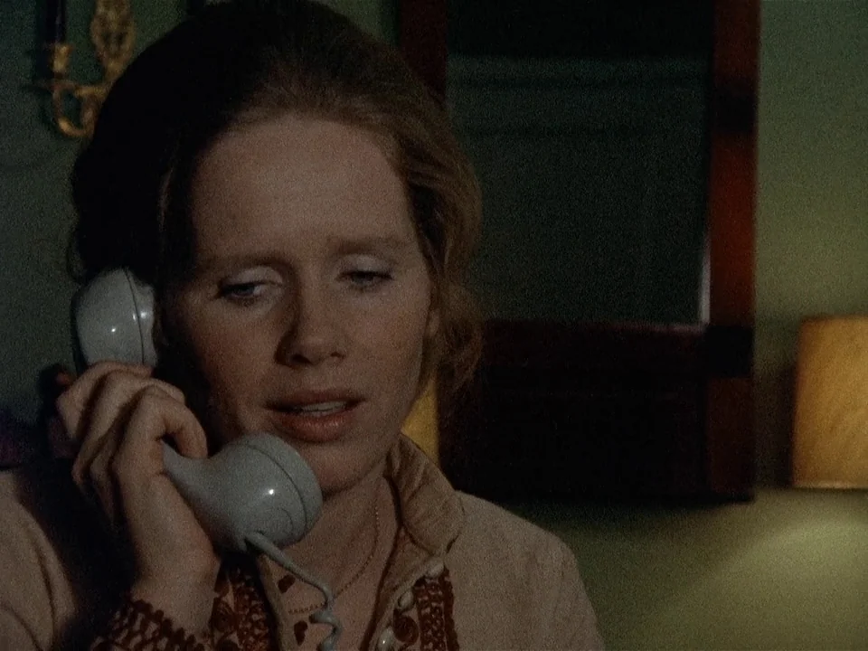 Scenes from a Marriage (1973) movie still: closeup — A dimly lit interior room with a lamp glowing in the background. A woman in a beige shirt holds…