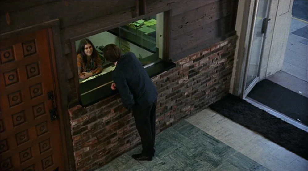 Five Easy Pieces (1970) movie still: wide — A lobby features a dark wood paneled wall and a brick base section. A man stands at a service window…
