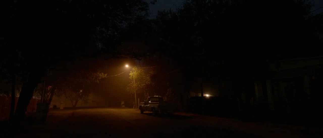 Song to Song (2017) movie still: establishing — A dark residential street is shrouded in evening shadows and ambient haze. A solitary pickup truck…