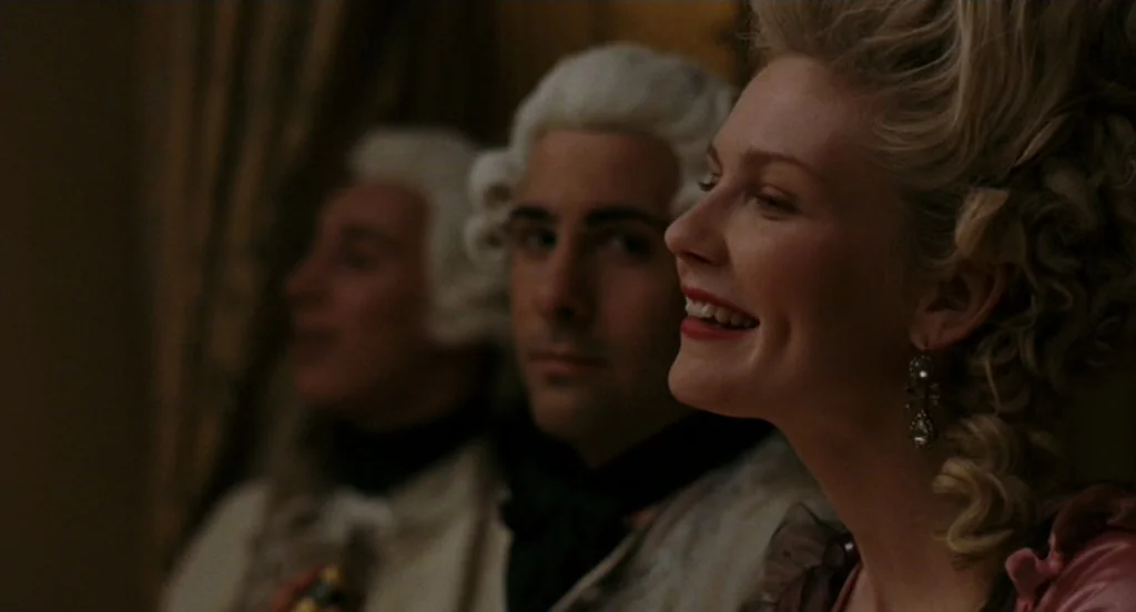 Marie Antoinette (2006) movie still: medium — A dimly lit, formal venue with gold-toned drapery in the background. Three people wearing powdered…