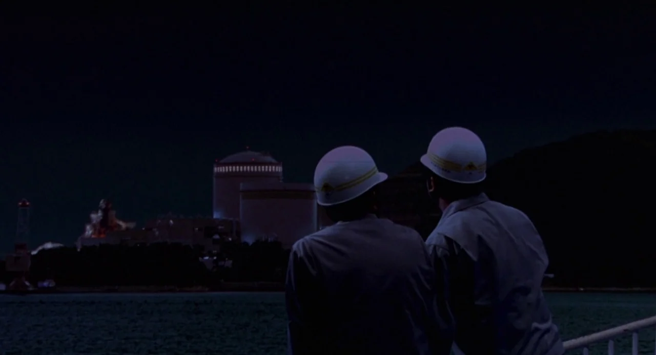 Godzilla vs. Destoroyah (1995) movie still: medium — A dark waterfront at night with a large industrial complex in the distance. Two men wearing…