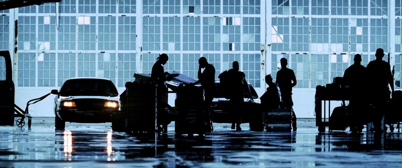Bad Boys II (2003) movie still: wide — A vast industrial hangar with a multi-paned glass wall background is filled with equipment. Multiple…
