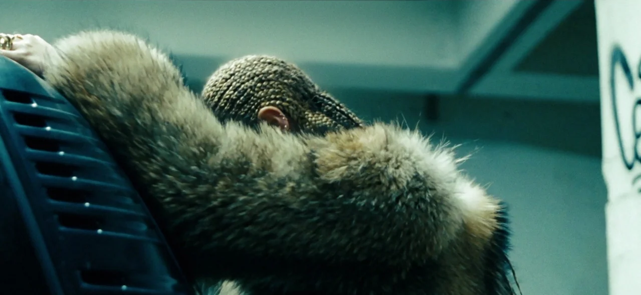 Lemonade (2016) movie still: closeup — A dimly lit concrete parking structure shows a person leaning against a dark vehicle. The person faces away…