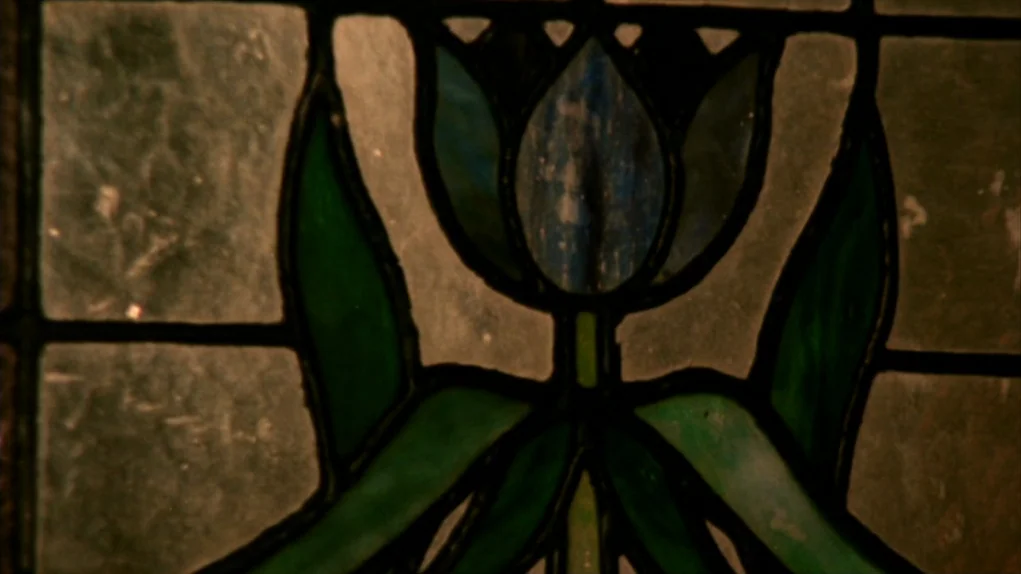 Face to Face (1976) movie still: closeup — A close-up view of a leaded stained glass window featuring a floral motif. Deep blue and forest green…