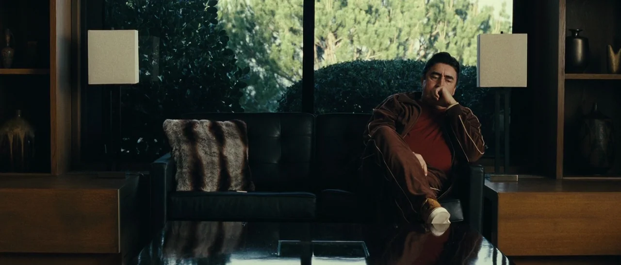 Message From The King (2016) movie still: medium — A dark living room features a black leather sofa positioned before a large glass window. An…