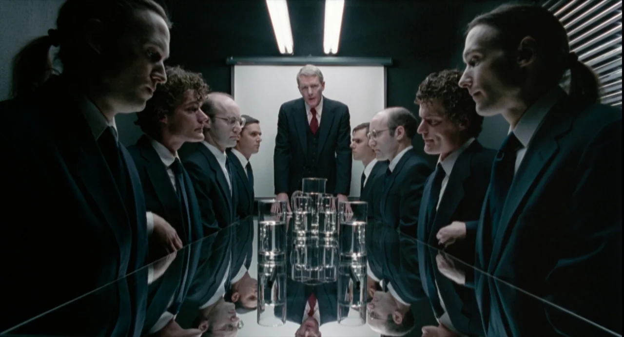 The Doom Generation (1995) movie still: medium — A dark, modern conference room features a highly reflective black table surface. Eight men in dark…