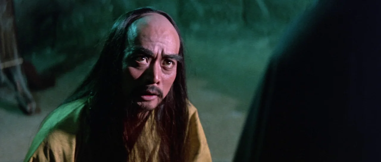 The Legend of the 7 Golden Vampires (1974) movie still: medium — A dimly lit room with stone-like walls illuminated by a green light source. An…