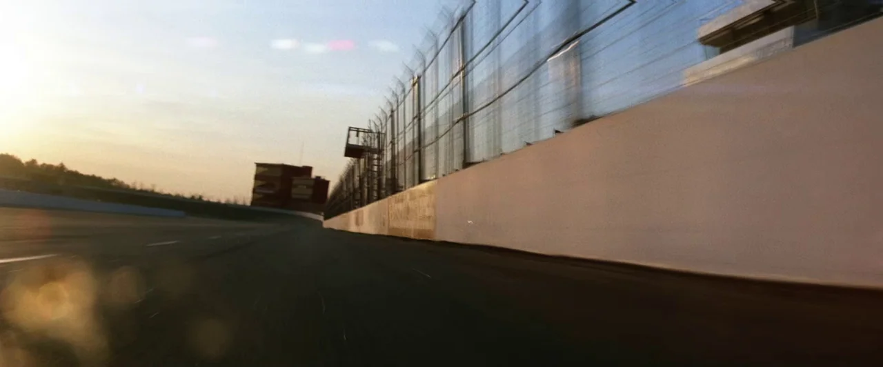 Days of Thunder (1990) movie still: establishing — A low-angle view travels rapidly along the white concrete barrier of a large racetrack. A tall…