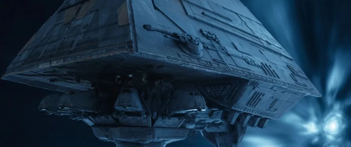 Andor (2022) movie still: establishing — A massive metallic spacecraft moves forward against a dark, featureless expanse of deep space. Bright blue…