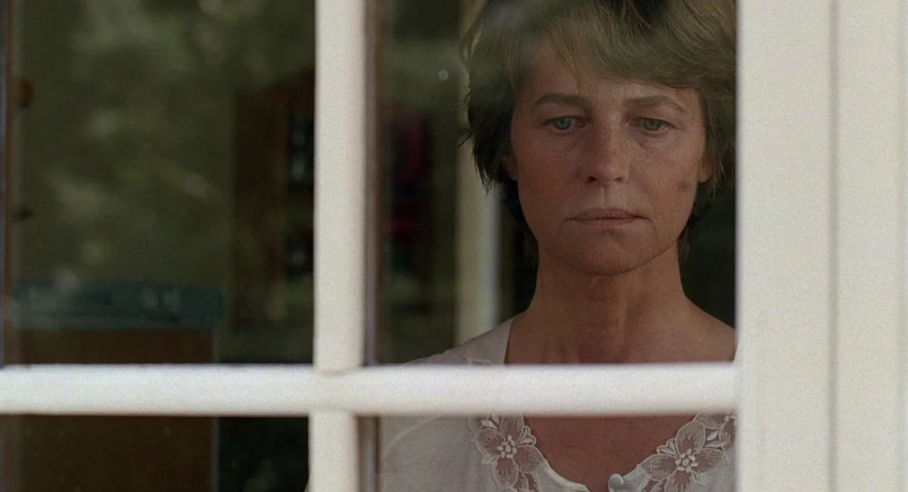 Swimming Pool (2003) movie still: closeup — A woman stares through the glass panes of a window frame from inside. The room is dimly lit behind her…