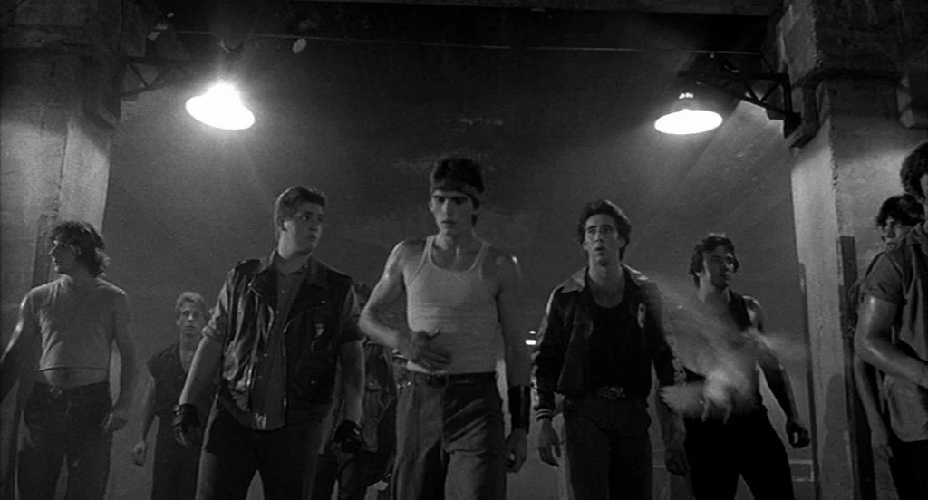 Rumble Fish (1983) movie still: fullbody — A group of men walks toward the camera through a concrete municipal underpass. Intense artificial light…