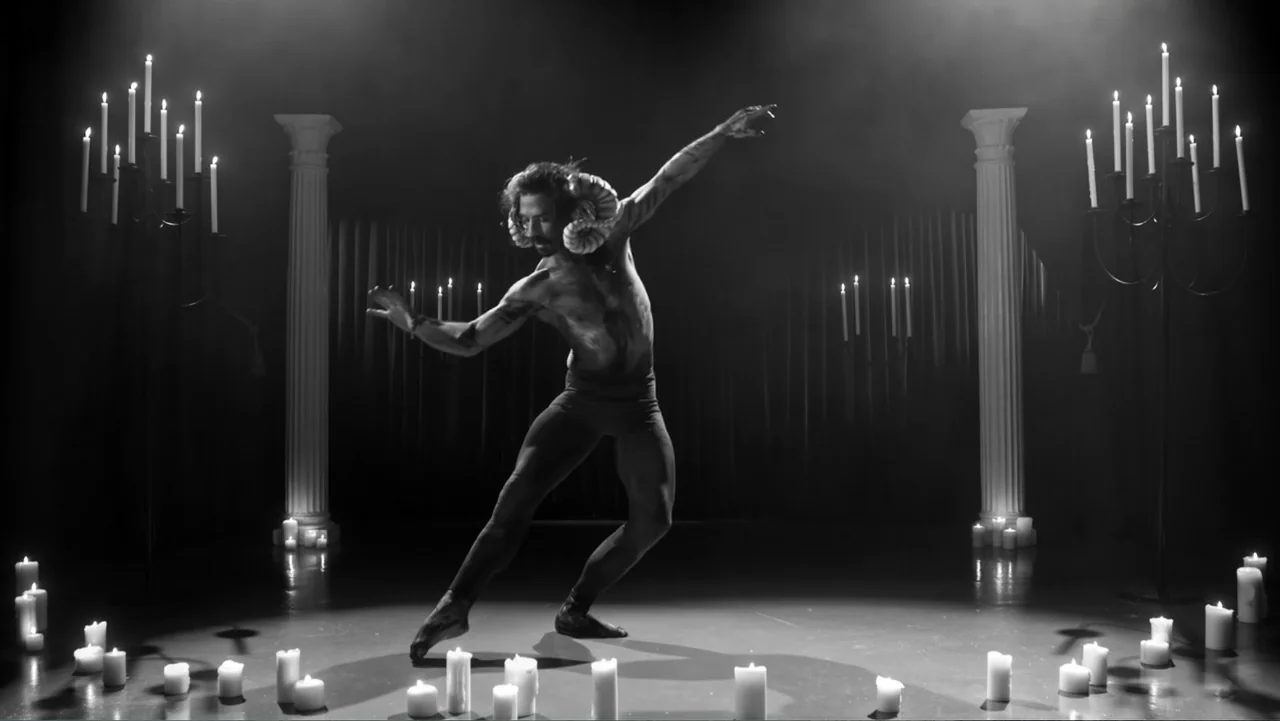 The Witch of Kings Cross (2020) movie still: fullbody — A dark, candlelit space is framed by two white classical pillars on either side. A man with…