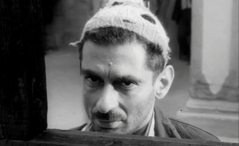 Cairo Station (1958) movie still: closeup — A man peers over a wooden partition in an outdoor area. He wears a knit cap and looks forward at the…