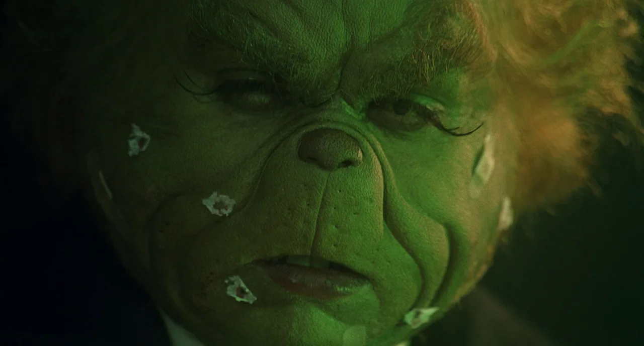 How The Grinch Stole Christmas (2000) movie still: closeup — A close-up of a green creature with wrinkled skin and small bandages on cheeks. The…