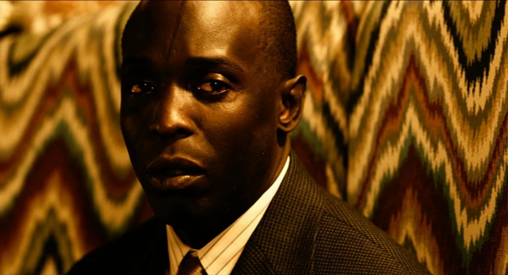 Life During Wartime (2009) movie still: closeup — A man sits within a booth lined with distinct zigzag-patterned fabric upholstery. The lighting…