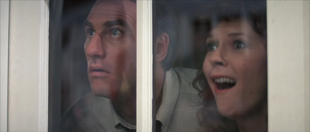 Poltergeist II: The Other Side (1986) movie still: closeup — A man and a woman appear behind a window frame pane. They look through the glass with…